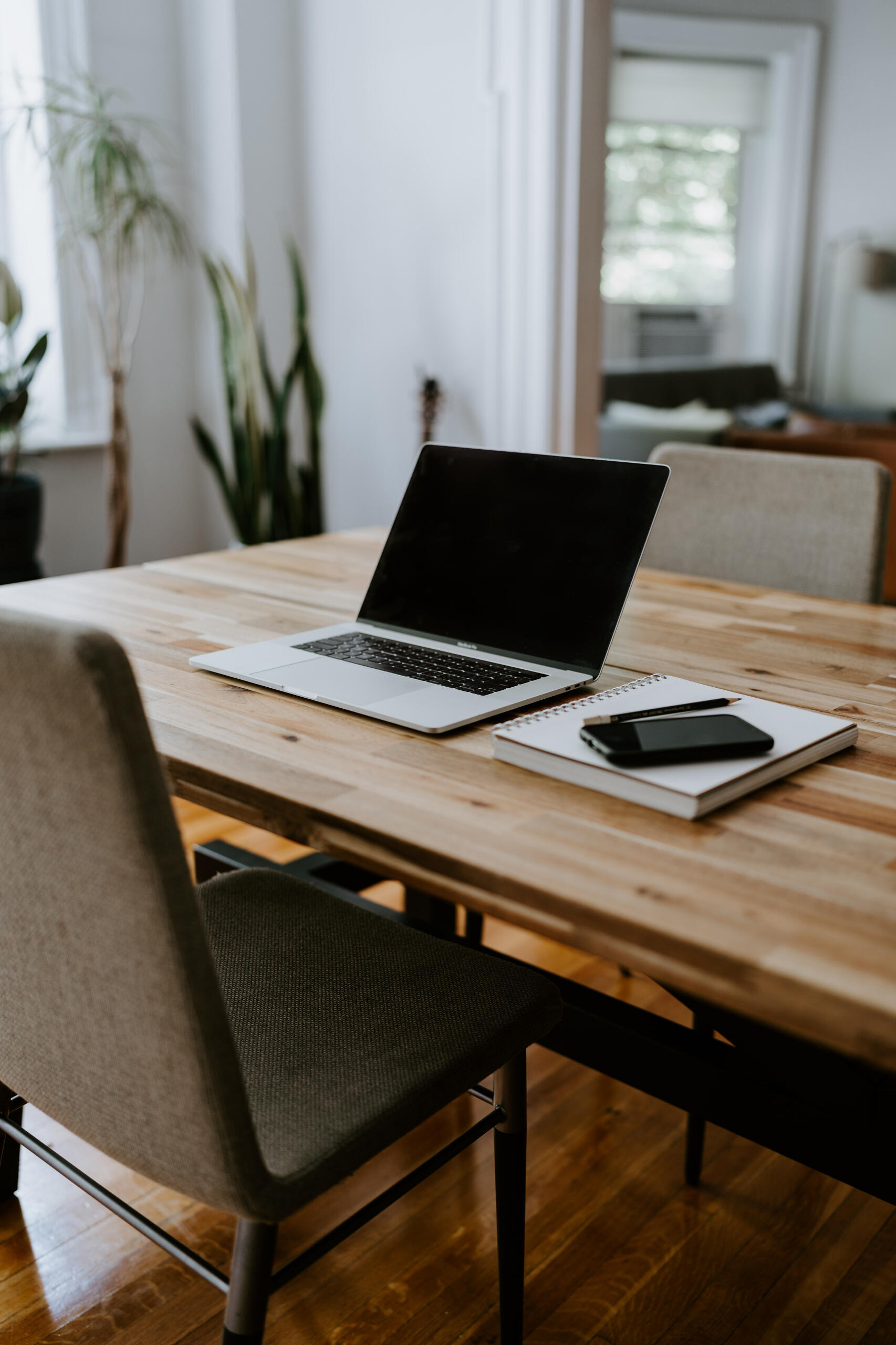 Laptop and notebook on a wooden table with seating in a bright workspace